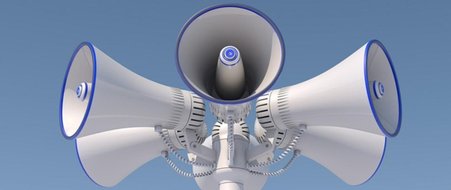 Na zdjęciu widać  syrenę alarmową składającą się z pięciu głośników skierowanych na wszystkie kierunki świata. Głośniki są w kolorze niebiesko białym.