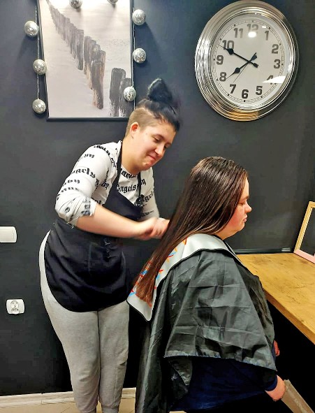 Wychowanka Młodzieżowego Ośrodka Wychowawczego im. Janusza Korczaka w Kwidzynie czesze osobie z niepełnosprawnością w pracowni fryzjerskiej