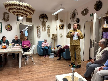 Kapitan Krzysztof Skoczek w mundurze strażaka prowadzi prelekcję w głównej sali Dziennego Domu Pobytu Seniora w Kwidzynie