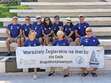 Członkowie Pomorskiego Stowarzyszenia Żeglarzy Niepełnosprawnych pozują do zdjęcia.