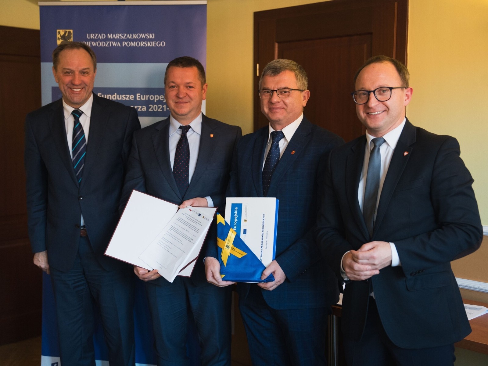 Zdjęcie pamiątkowe po podpisaniu umowy. Od lewej stoją: Mieczysław Struk, Tomasz Frejangiel, Tomasz Pisarek i Marcin Skwierawski. Tomasz Frejangiel prezentuje podpisaną umowę, a Tomasz Pisarek dyplom i flagę Unii Europejskiej