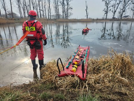 Strażacy przeprowadzają akcję ratunkową na zamarzniętym akwenie, stosując odpowiednie techniki w trudnych warunkach lodowych.