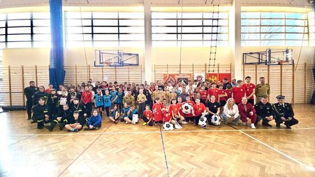 Zdjęcie przedstawia dzieci, młodzież i osoby dorosłe podczas powiatowego turnieju halowej piłki nożnej. Zdjęcie wykonane zostało na hali sportowej. 