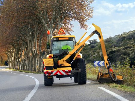 Zdjęcie ilustracyjne do treści artykułu przedstawia traktor koszący pobocze drogi.