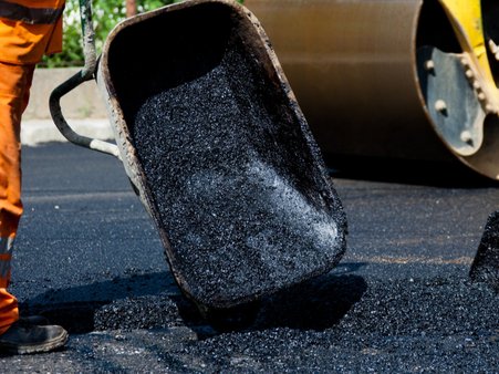 Zdjęcie ilustracyjne do treści artykułu przedstawia pracownika naprawiającego nawierzchnię drogi.