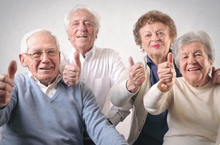 zdjęcie przedstawia czworo uśmiechniętych ludzi w podeszłym wieku, trzymających kciuki w górze. 