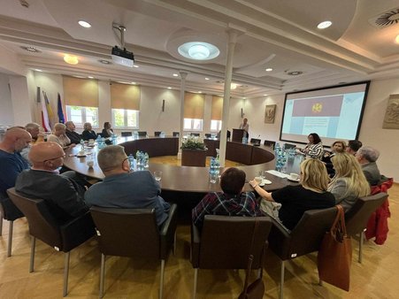 Zdjęcie przedstawia grupę siedzących osób przy okrągłym stole. 