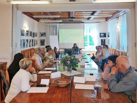 Uczestnicy siedzą przy jednym stole i słuchają prowadzącej szkolenie.