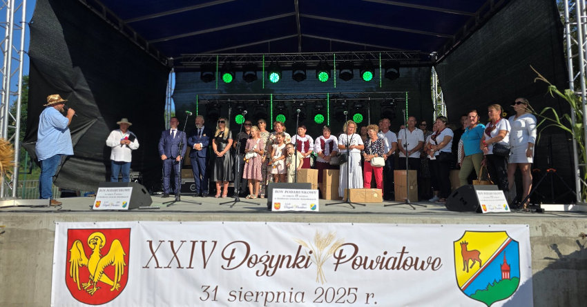 Gospodarze, zaproszeni goście oraz nagrodzone i wyróżnione osoby stoją na scenie, na pierwszym planie baner z napisem: XXIV Dożynki Powiatowe, 31 sierpnia 2025.