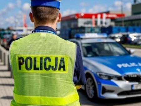 zdjęcie przedstawia policjanta stojącego plecami. W tle widać radiowóz