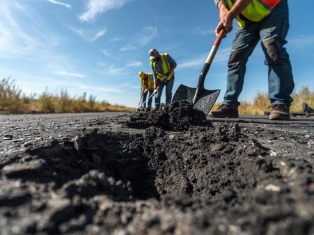 Zdjęcie przedstawia trzech robotników z łopatami, łatających dziury w drodze