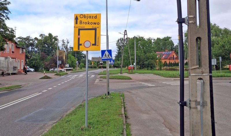Znak z informacją o drodze objazdowej do Brokowa przez Brachlewo i Dubiel, ustawiony przy skrzyżowaniu w terenie zabudowanym. W tle widoczne są budynki mieszkalne, zieleń i oznakowanie drogowe.