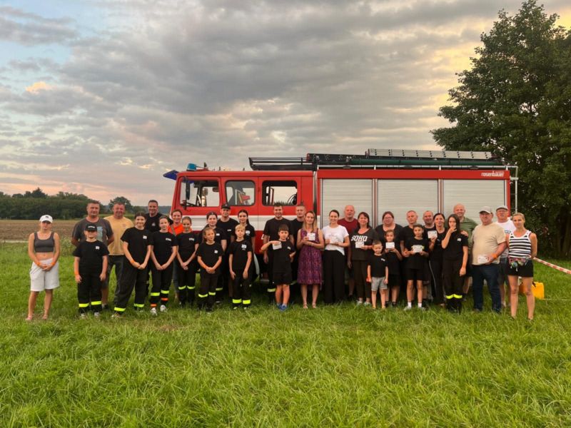 zdjęcie przedstawia stojących ludzi i strażaków na tle wozu strażackiego.