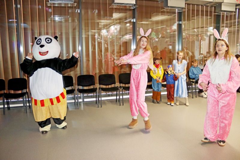 Animatorzy prowadzą zabawę, a w tle dzieci biorą udział w tańcach i cieszą się atmosferą karnawałowego balu.