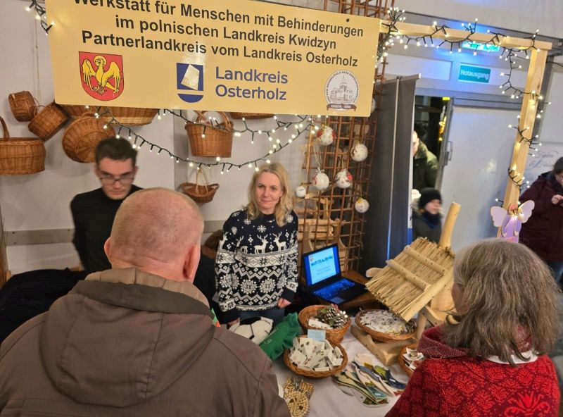 Uczestnicy WTZ prowadzący swoje stoisko na Jarmarku Bożonarodzeniowym w Osterholz-Scharbeck, oraz osoby zainteresowane wyrobami.