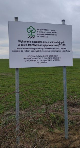 tablica informacyjna przy drodze na tle pola.
